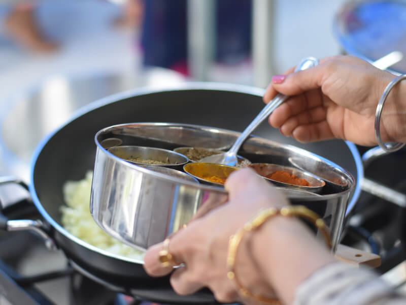 A person adding spices to a frying pan.